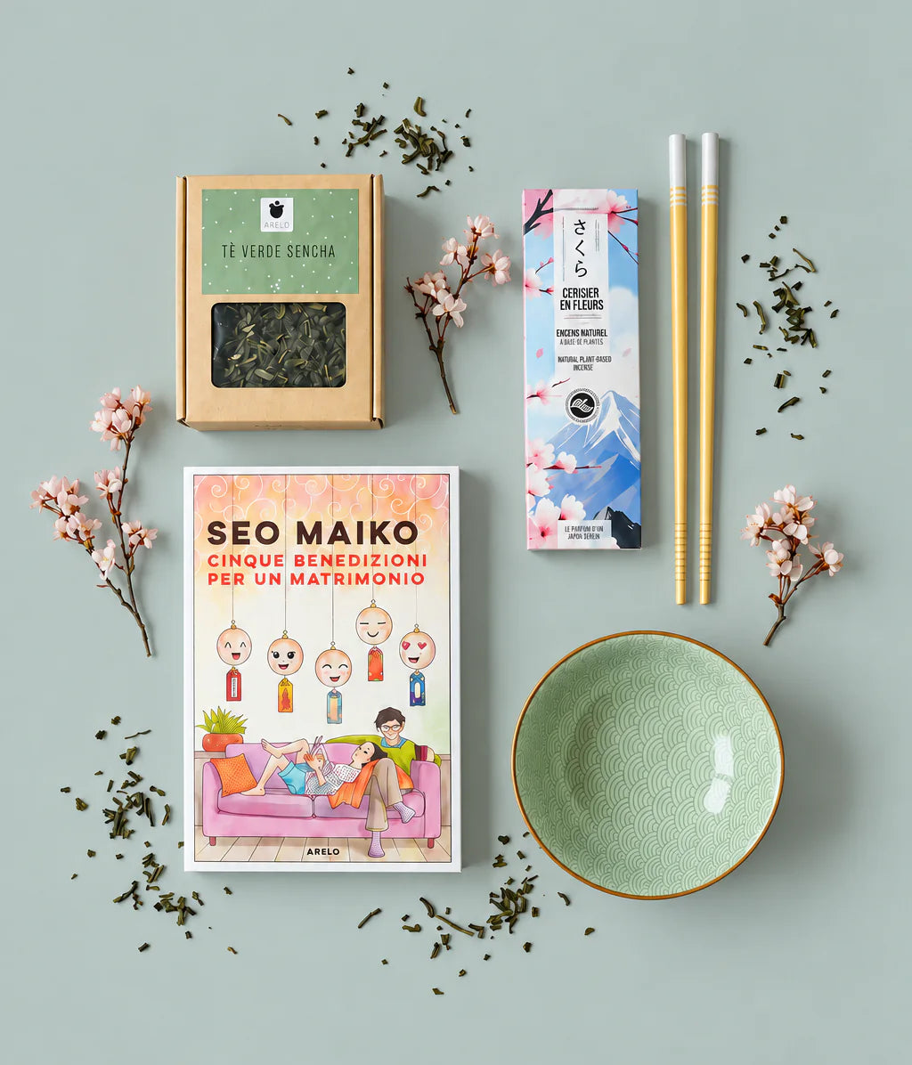 Vista dall’alto: il libro Cinque benedizioni per un matrimonio di Seo Maiko con il tè verde sencha, i bastoncini d’incenso ai fiori di ciliegio, una ciotola verde, bacchette e rametti di ciliegio in fiore