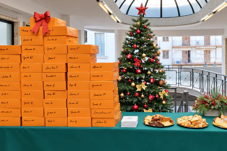 Decine di box Bookted arancioni con il nome di ognuno scritto a mano, su un tavolo accanto all’albero di Natale di un ufficio