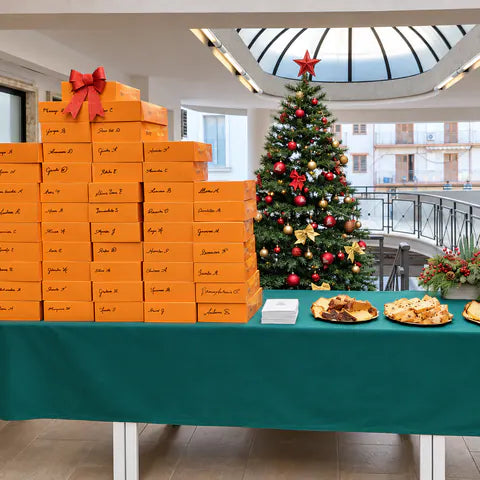 Decine di box Bookted arancioni con i nomi scritti a mano, accanto all’albero di Natale di un ufficio