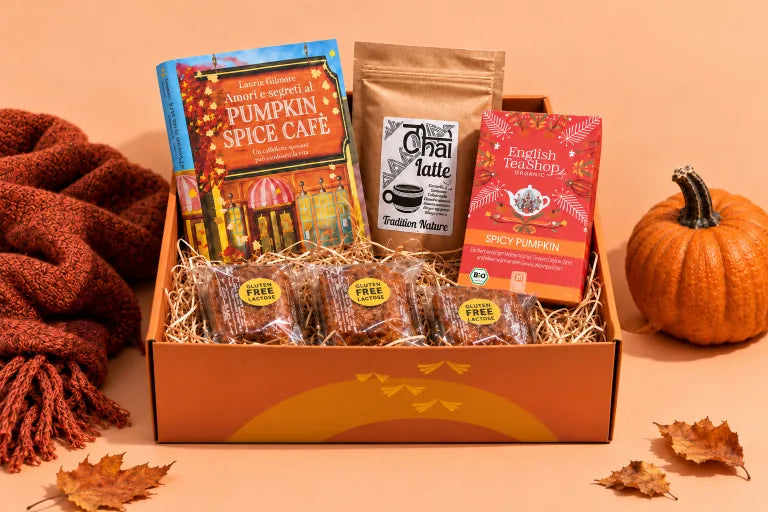 La box Bookted Amori e segreti al Pumpkin Spice Café con il romanzo di Laurie Gilmore, chai latte, tè Spicy Pumpkin e tre tortine alla zucca, accanto a un plaid e una zucca decorativa