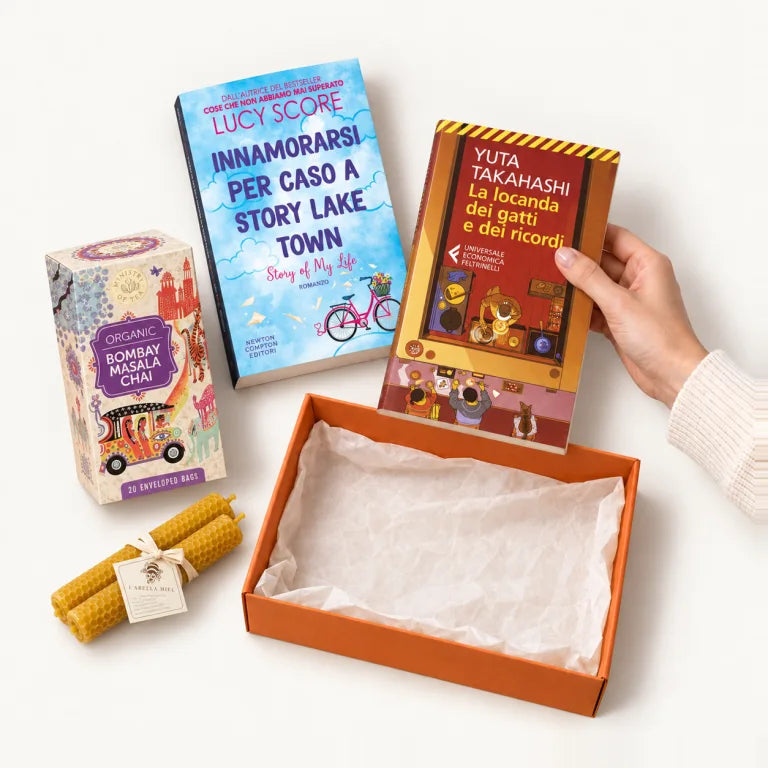 Una mano sceglie un libro accanto a una box Bookted vuota, con tè e candele