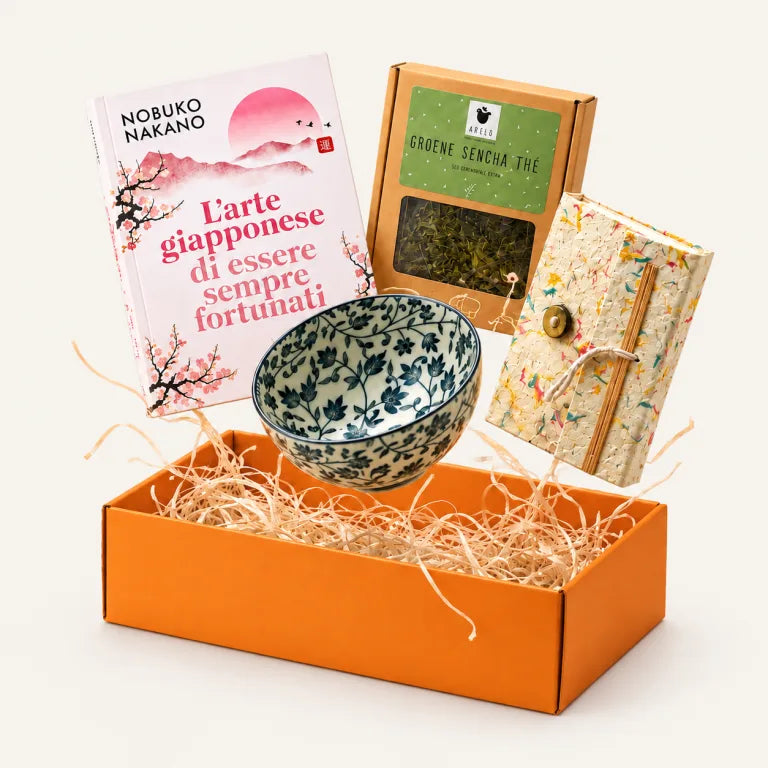 I pezzi di una box personalizzata sopra la scatola arancione aperta: il libro, il tè, una ciotola e un quaderno