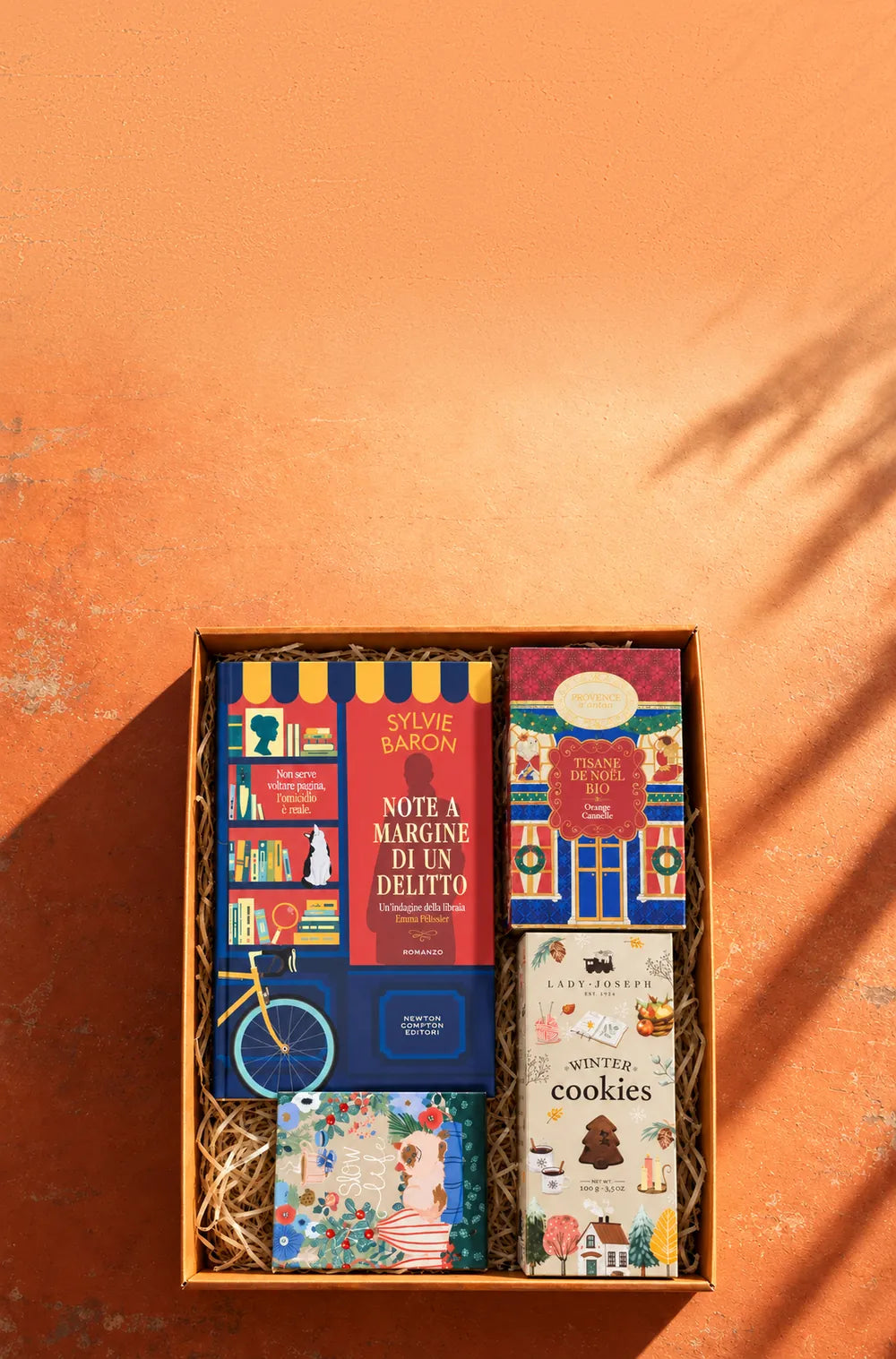 Una box Bookted aperta vista dall’alto, su un muro arancione con l’ombra di una pianta