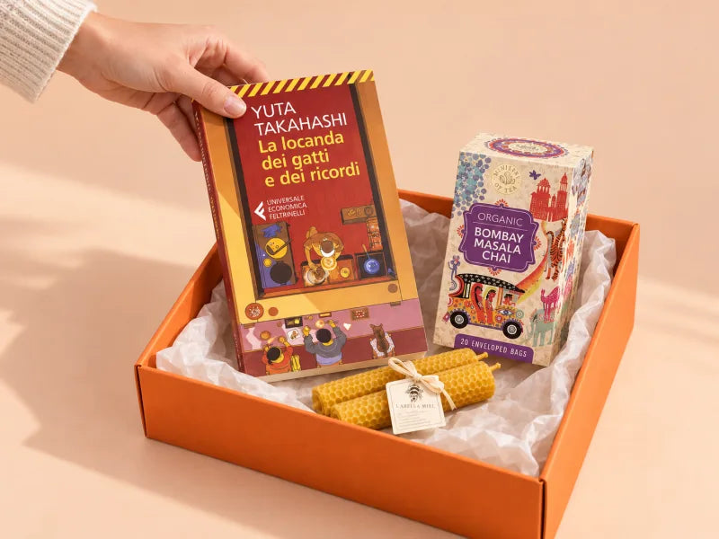 Una mano posa «La locanda dei gatti e dei ricordi» nella box arancione, accanto al tè e alle candele