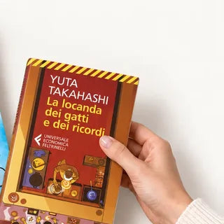 Una mano tiene «La locanda dei gatti e dei ricordi» sopra la box